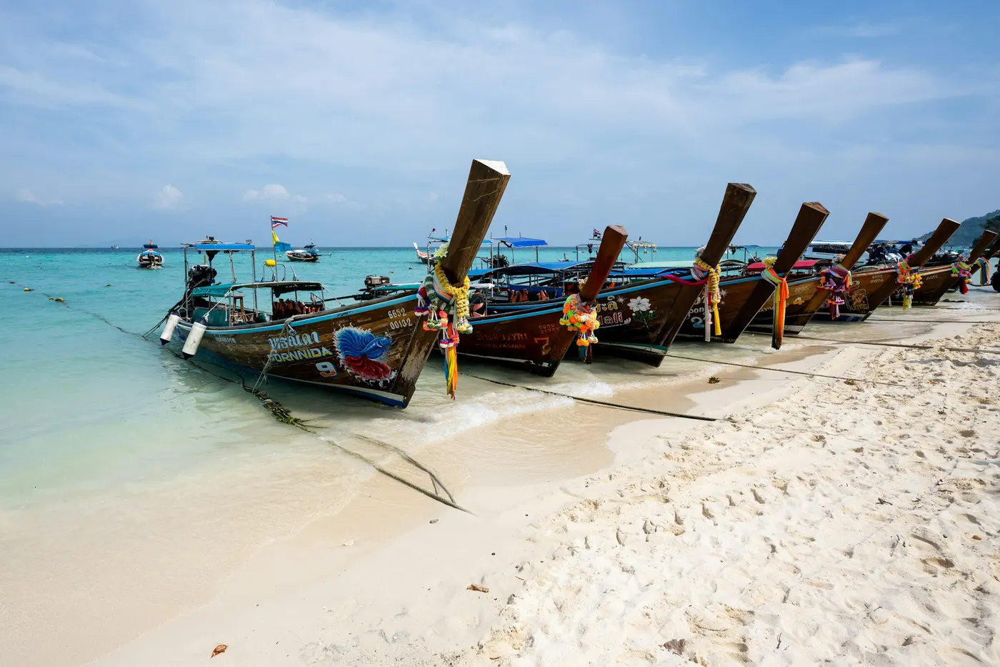 A row of longtail boats on a white-sand beach in the Phi Phi Islands
